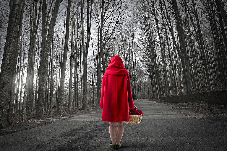 Eine Frau im roten Mantel steht im Wald mit Rücken zur Kamera. Das "Rotkäppchen-Syndrom" steht für uralte Ängste, die Menschen gegenüber dem Wolf hegen. (Foto: olly/AdobeStock )